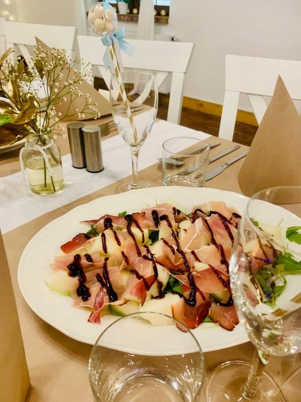 na brązowym obrusie danie z szynką i sosem balsamico na białym talerzu, obok brązowe serwety