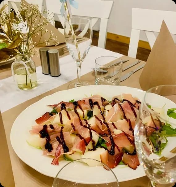 biały talerz ze przyprawionym daniem, obok kieliszki i elegancka zastawa